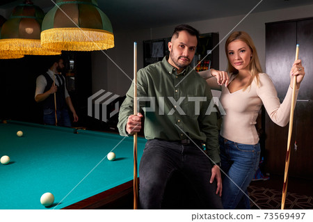 young caucasian beautiful couple standing near the pool billiard table young caucasian beautiful couple standing near the pool billiard table 73569497
