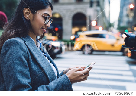 Focused delighted female in eyeglasses typing on mobile Focused delighted female in eyeglasses typing on mobile 73569867