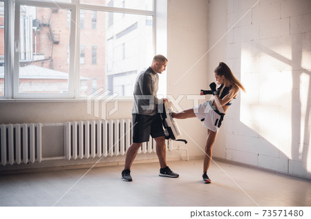Training of a professional female fighter. The girl works out a kick on the paw, which is held by her individual trainer 73571480