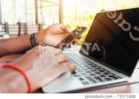 man person working with laptop computer and reading message from modern smart phone 73571886