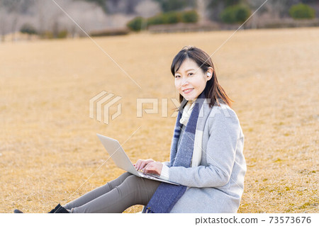 A woman sitting on the grass in the park and typing while listening to music A woman sitting on the grass in the park and typing while listening to music 73573676