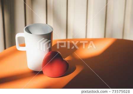 heart shape rubber and mug on orange table 73575028