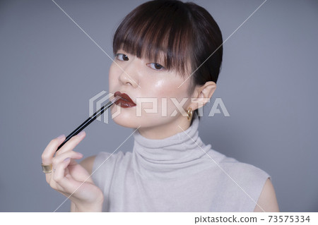 Woman applying brown lipstick 73575334