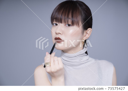 Woman applying brown lipstick 73575427