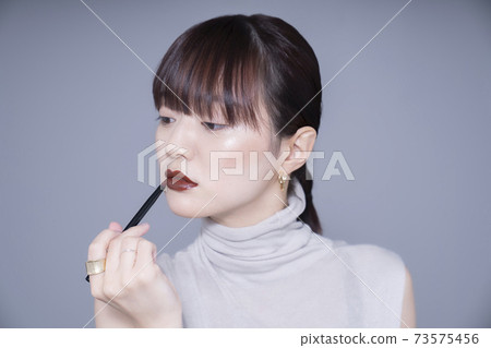 Woman applying brown lipstick 73575456