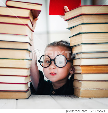 Cute little girl taking a book from top of books tower. Reading and kids education concept 73575571