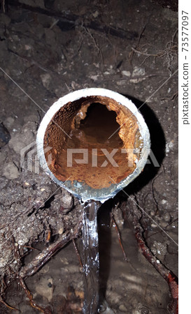 Old broken rusty water pipe underground with running water during out 73577097