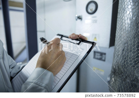 Male worker filling out an inspection sheet at the factory 73578892