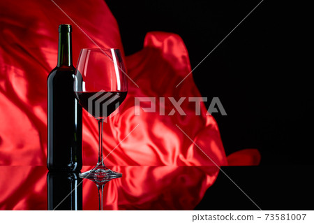 Wineglass and bottle of red wine on a black reflective background. Wineglass and bottle of red wine on a black reflective background. 73581007