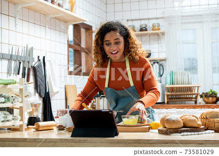 African American woman learning online cooking via tablet in kitchen at home 73581029