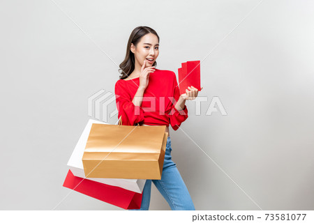 Smiling beautiful Asian woman holding shopping bags and red envelopes Smiling beautiful Asian woman holding shopping bags and red envelopes 73581077