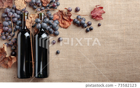 Red wine bottles and  grapes with dried up vine leaves. 73582123