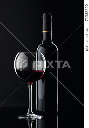 Bottle and glass of red wine on a black background. 73582200