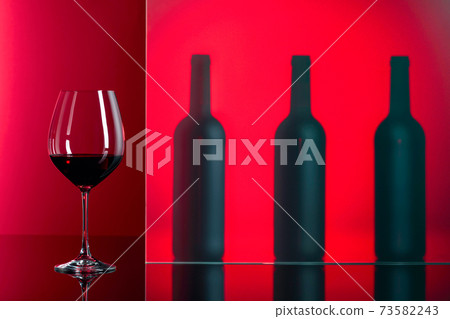 Bottles and glass of red wine on a red background. 73582243