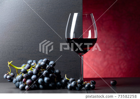 Blue grapes and glass of red wine on a black table. 73582258
