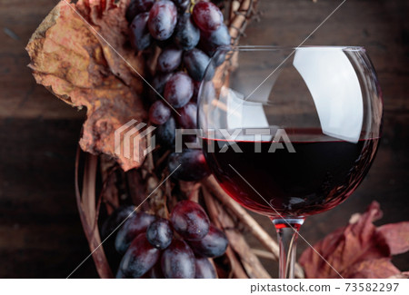 Glass of red wine with grapes and dried  leaves. 73582297