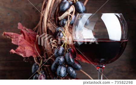 Glass of red wine with grapes and dried vine leaves. 73582298