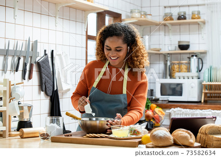 African American woman enjoying cooking while listening to music with earphone  73582634