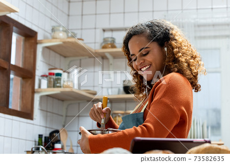 Happy young African American woman cooking and listening to music Happy young African American woman cooking and listening to music 73582635