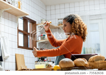 Happy young African American woman enjoying herself while cooking in kitchen Happy young African American woman enjoying herself while cooking in kitchen 73582638