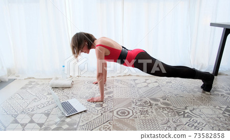 Woman doing push-ups home in front of laptop 73582858
