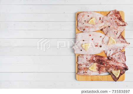 Raw squid carcass with spices and lemon ready for cooking on a wooden cutting board. copy space. Top view 73583897