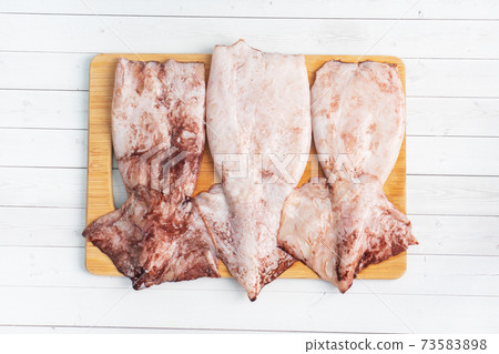 Raw squid carcass with spices ready for cooking on a wooden cutting board. Top view 73583898