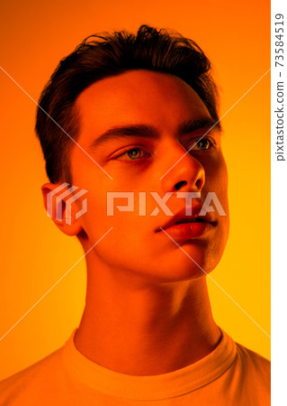 Handsome caucasian man's portrait isolated on orange studio background in neon light, monochrome Handsome caucasian man's portrait isolated on orange studio background in neon light, monochrome 73584519