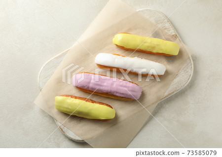Board with eclairs with custard on white textured background 73585079