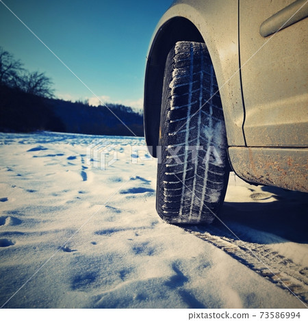 Car in winter in the snow. Winter tires. Winter landscape with sun and blue sky in the background. Car in winter in the snow. Winter tires. Winter landscape with sun and blue sky in the background. 73586994