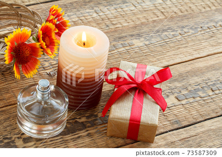 Perfume, gift box, candle and fresh flowers on wooden table. Perfume, gift box, candle and fresh flowers on wooden table. 73587309