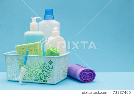 Bottles of dishwashing liquid in basket, sponges and brushes on blue background. 73587400