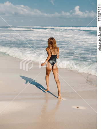 Attractive slim woman in black swimwear, caucasian model running at ocean beach 73587454