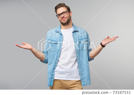 Portrait of confused clueless young man in jeans shirt standing over grey background Portrait of confused clueless young man in jeans shirt standing over grey background 73587531