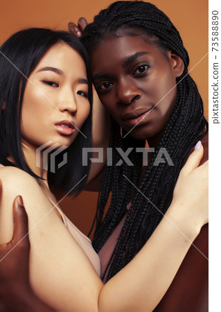 young pretty asian and afro woman posing cheerful together on brown background, lifestyle diverse nationality people concept 73588890