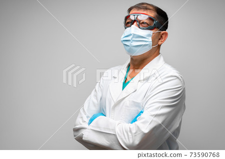 Senior male doctor in face mask standing against grey background Senior male doctor in face mask standing against grey background 73590768