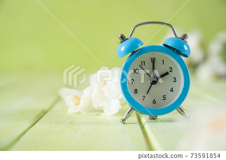 Spring time daylight saving concept - with alarm clock and flowers Spring time daylight saving concept - with alarm clock and flowers 73591854