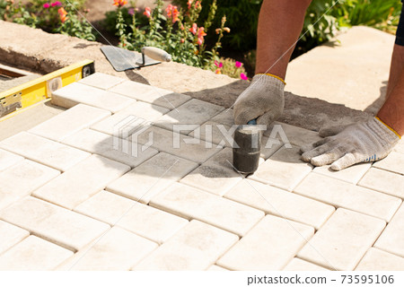 The master lays paving stones in layers. Garden brick pathway paving. Laying concrete paving slabs in house courtyard on sand foundation base 73595106