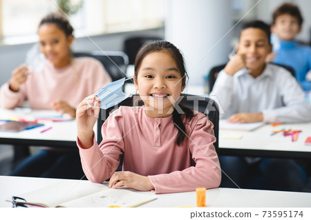 Smiling asian girl taking off disposable medical mask at classroom Smiling asian girl taking off disposable medical mask at classroom 73595174