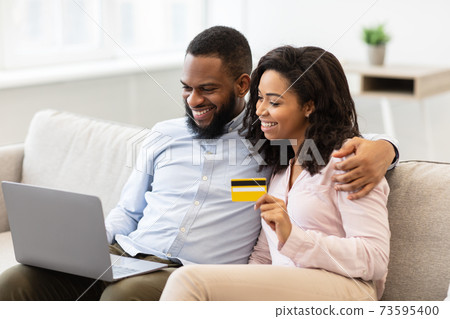 Black couple using computer and debit credit card at home 73595400