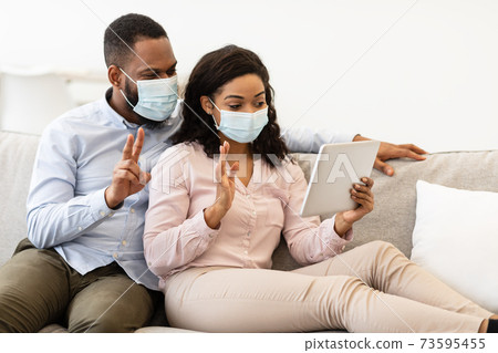 Black couple in masks waving to tablet during videocall Black couple in masks waving to tablet during videocall 73595455