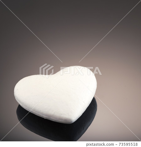 White 3d heart made of polystyrene, on a dark background with place for text. Artificial love concept, frozen heart. Studio photo. Valentine's Day. Side view 73595518