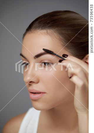 Eyebrows shaping. Portrait of beautiful girl with brow pencil. Close-up of young woman with professional makeup contouring brows with eyebrow pencil. Beauty cosmetic concept. Eyebrows shaping. Portrait of beautiful girl with brow pencil. Close-up of young woman with professional makeup contouring brows with eyebrow pencil. Beauty cosmetic concept. 73596438