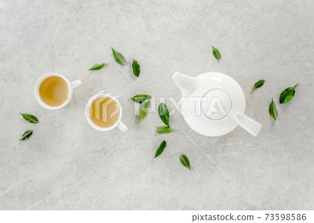 Herbal tea with two white tea cups and teapot, with green tea leaves. Flat lay, top view. Tea concept 73598586
