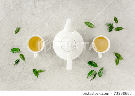 Herbal tea with two white tea cups and teapot, with green tea leaves. Flat lay, top view. Tea concept 73598693