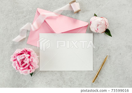 Mockup invitation, blank paper greeting card, pink envelope and peonies on gray stone table. Flower background. Flat lay, top view. 73599016