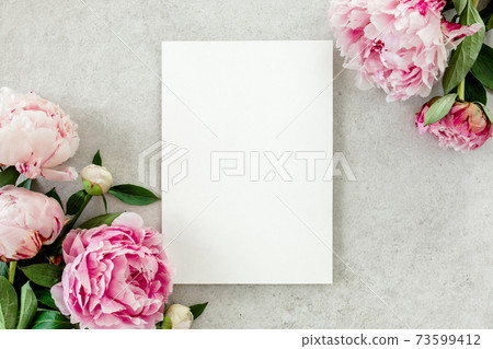 Mockup invitation, blank paper greeting card and peonies on gray stone table. Flower background. Flat lay, top view. 73599412