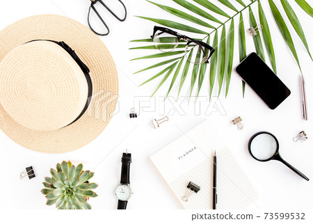 Top view home office desk. Workspace with straw hat, glasses, retro camera, notepad and tropical palm leaf on white background. Flat lay, top view. 73599532