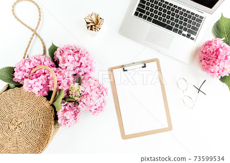 Stylized women's desk. Workspace with clipboard, laptop, bouquet hydrangea, accessories on white background. Flat lay. Top view. 73599534