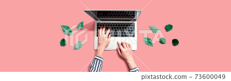 Person using a laptop computer with green leaves 73600049